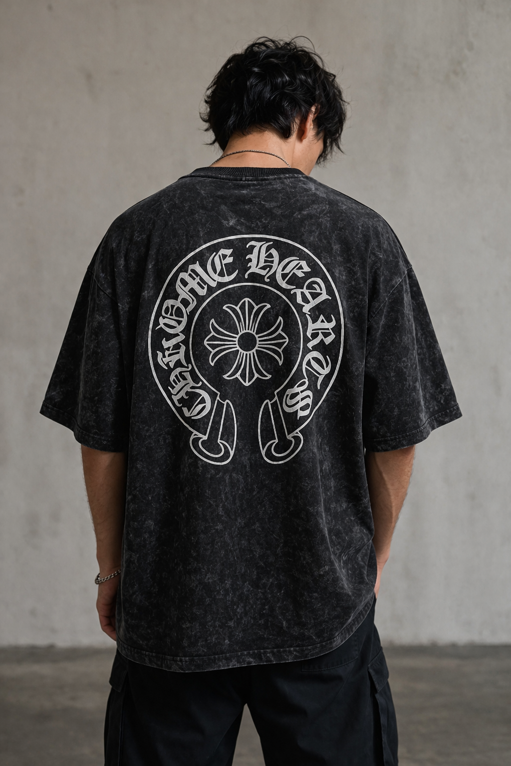 Person wearing a black t-shirt with a white graphic design on the back against a gray wall.